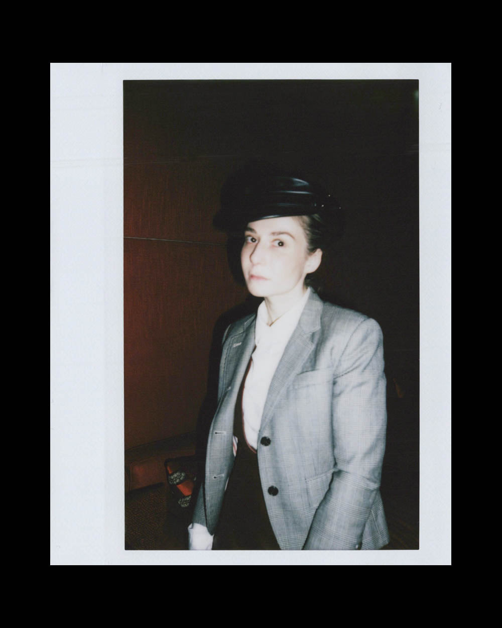 A person wearing a gray blazer and black hat poses against a dark, out-of-focus background.