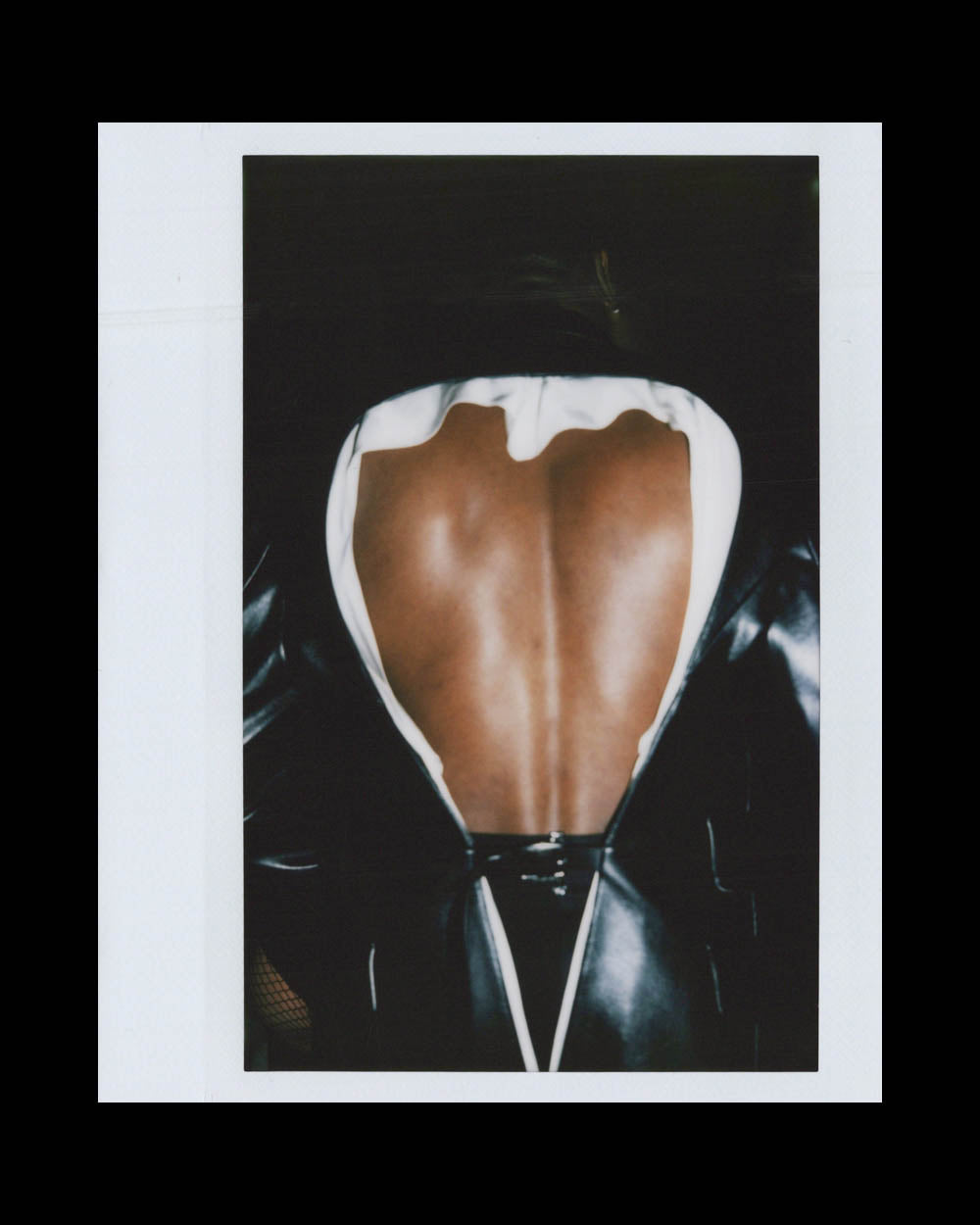 A person wearing a black shiny outfit with a large open back showing smooth skin and a defined spine.