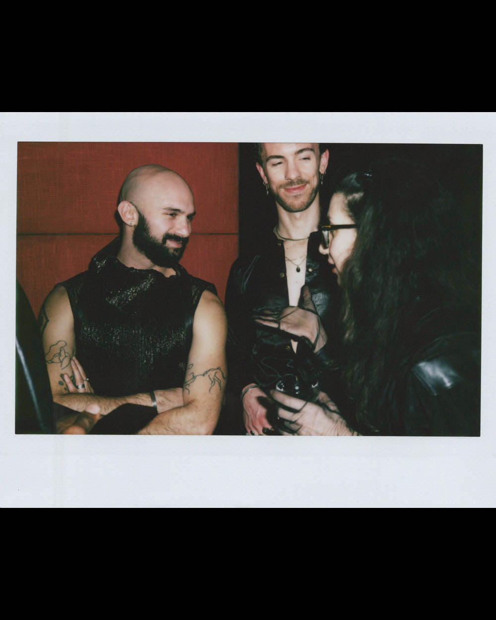 Three people in dark clothing engaged in conversation in a dimly lit indoor setting.