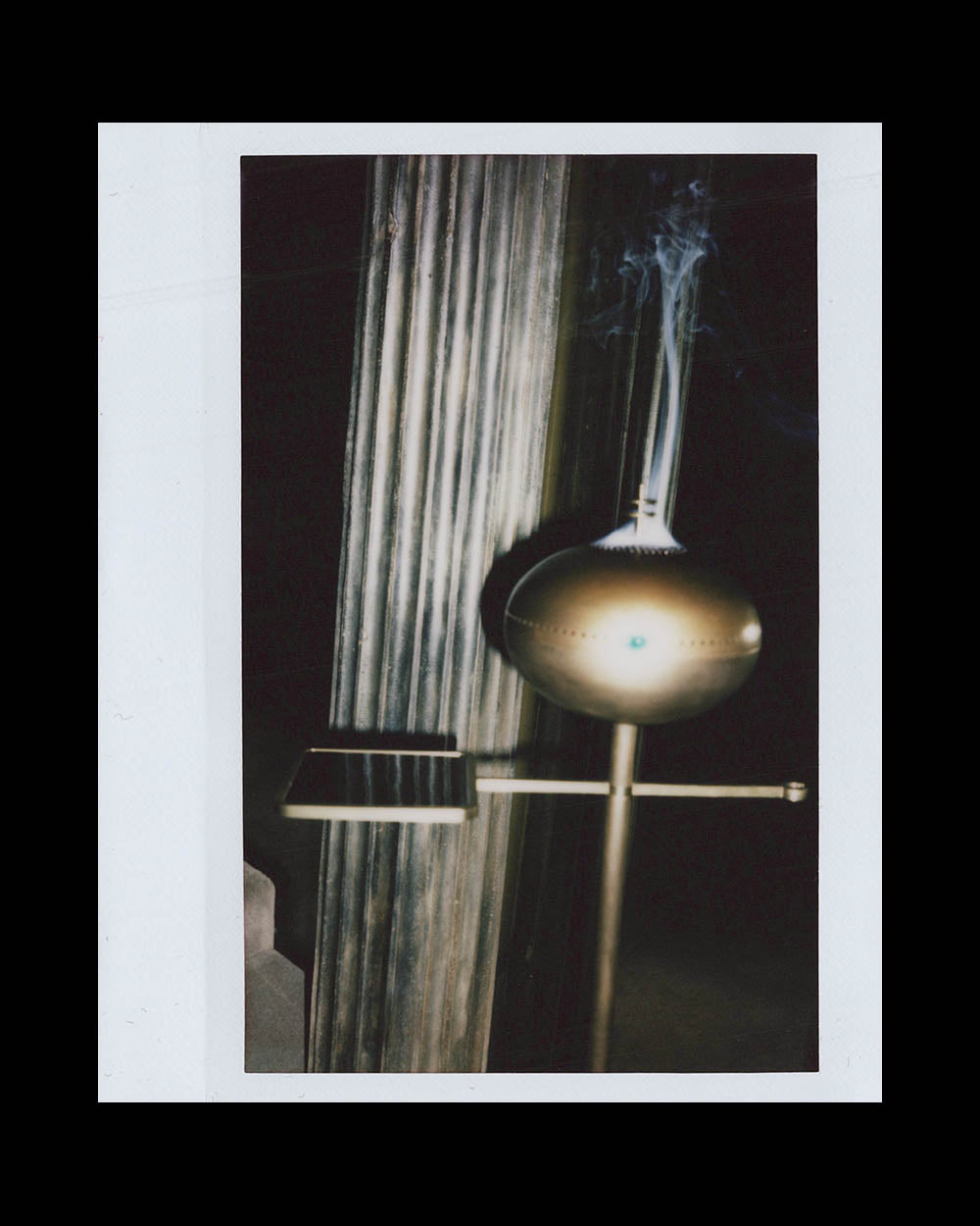 Bronze incense burner emitting smoke near a fluted column in a dimly lit space.