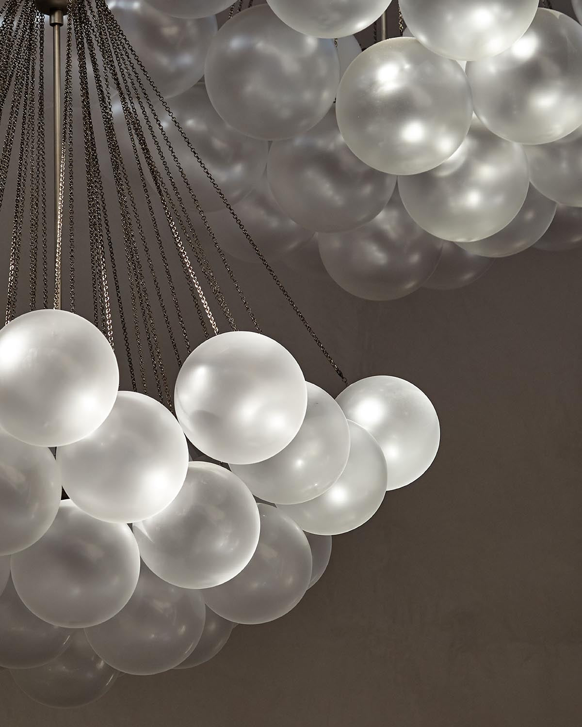 Close-up of two modern pendant lights with clusters of frosted glass globes suspended by dark metal chains against a neutral background
