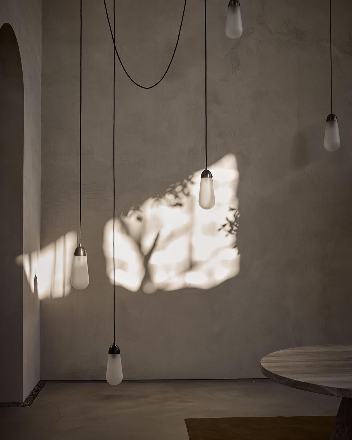 Minimalist interior with hanging pendant lights casting soft shadows of tree branches on a textured beige wall