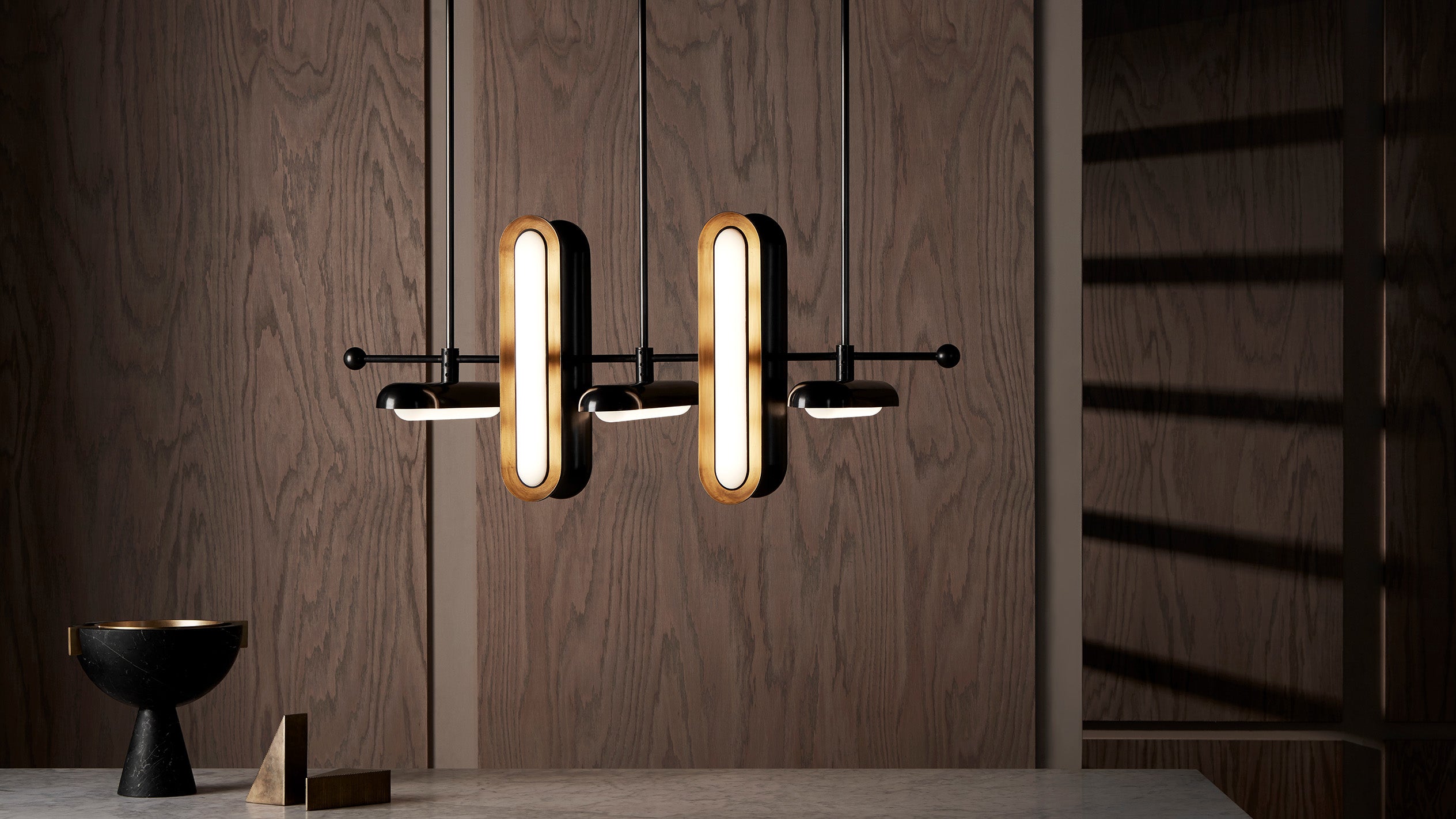 Modern pendant light fixture with elongated oval bulbs hanging against a dark wood paneled wall