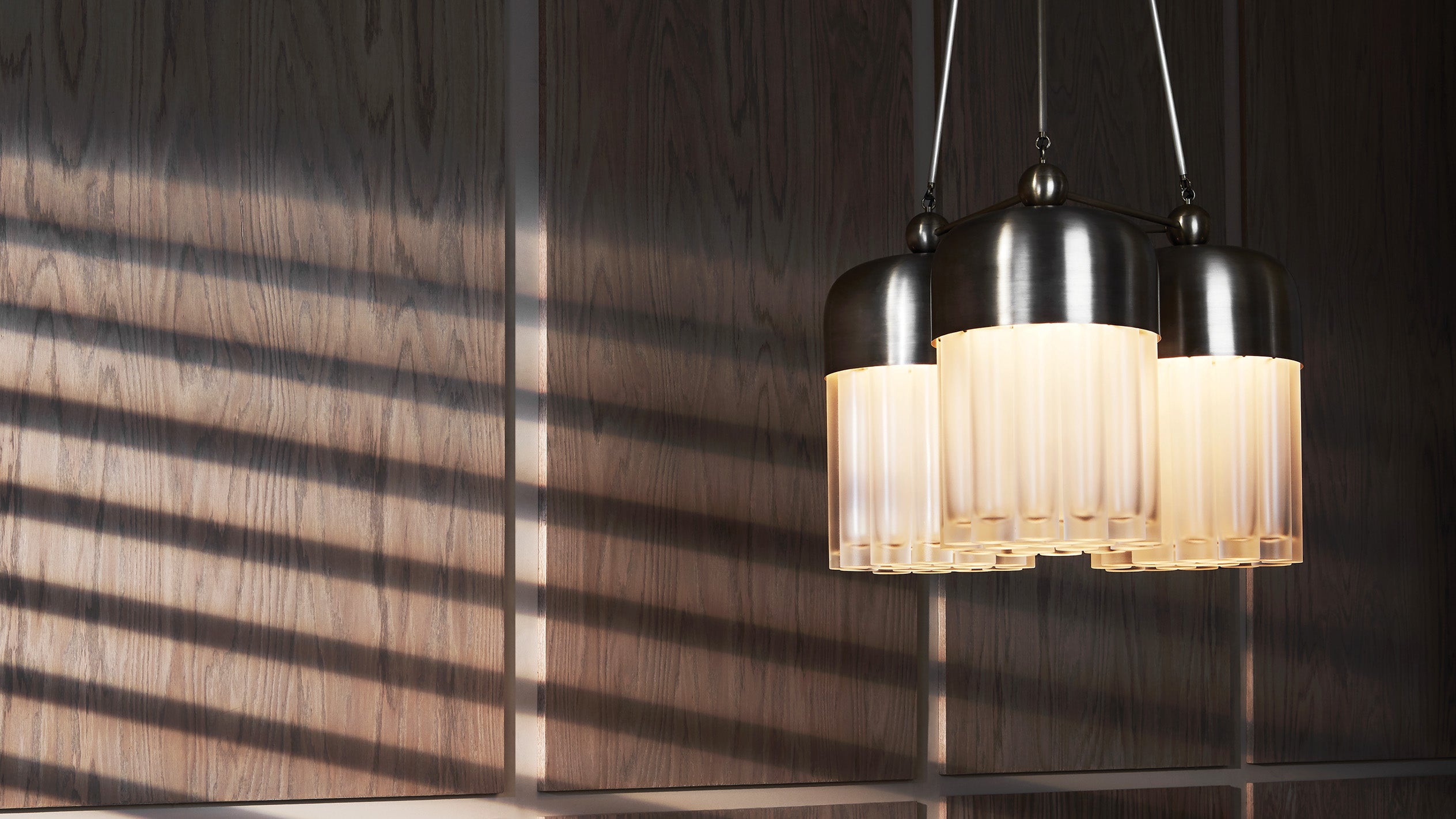 Cluster of three ribbed glass pendant lights with dark metal fixtures casting shadows on a wood-paneled wall