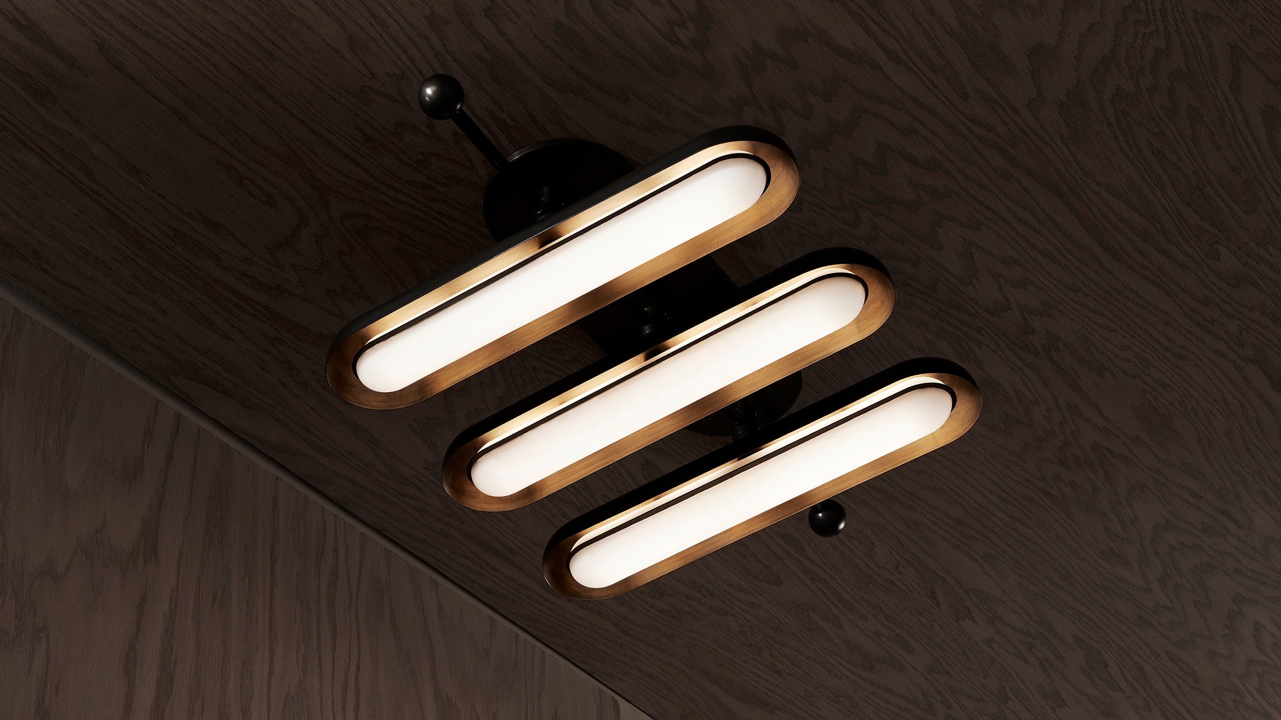 Modern ceiling light fixture with three elongated oval LED lamps mounted on a dark wooden surface
