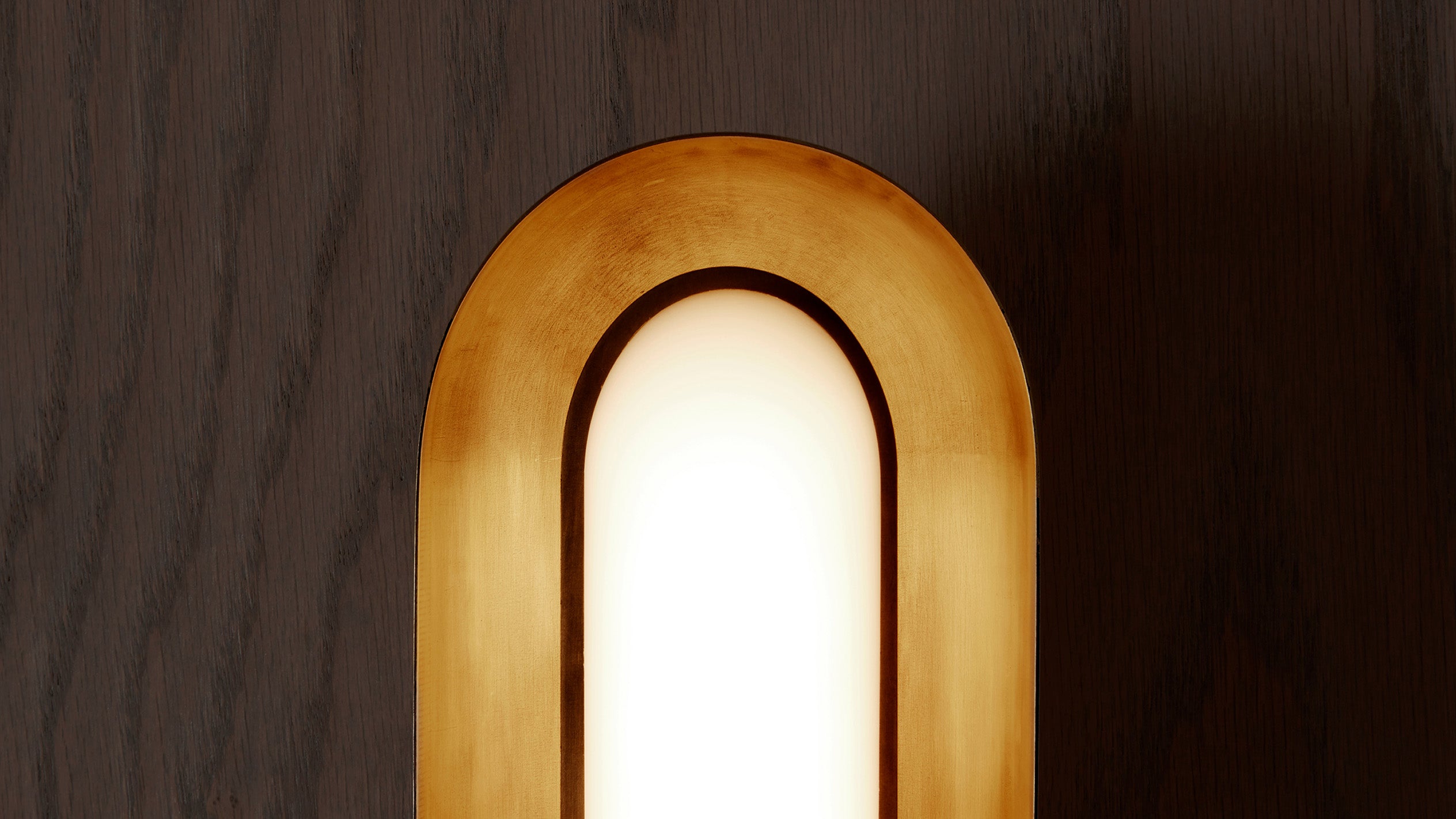 Close-up of an arched wall light with warm golden frame against dark wooden paneling background
