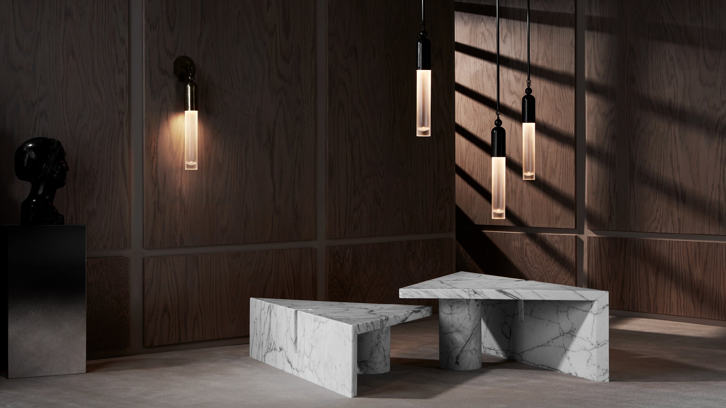 Minimalist interior with geometric white marble benches, dark wood panels, vertical pendant lights, and sculptural decor on floor