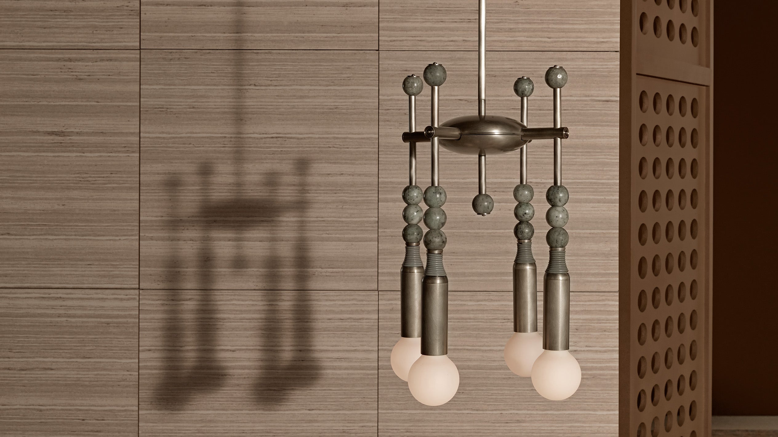 Minimalist metal pendant light fixture with spherical bulbs and decorative beads casting a shadow on a textured wooden wall