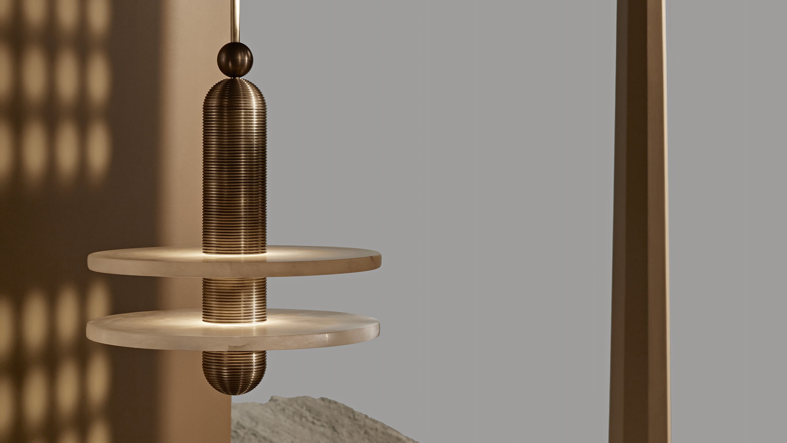 Bronze metallic pendant light with cylindrical shape hanging above two stacked circular shelves against neutral background