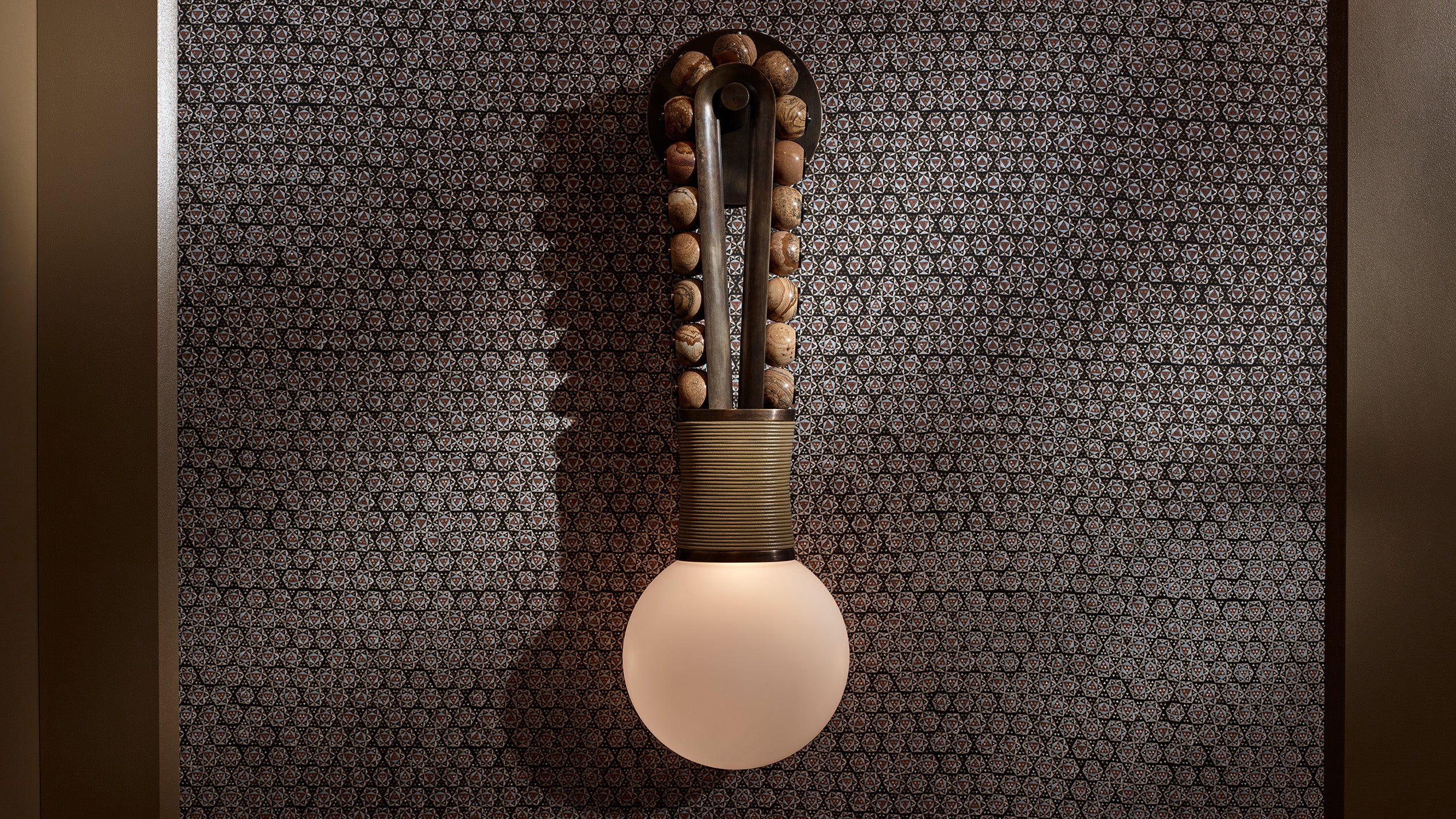 Wall-mounted light fixture with round bulbs and wooden bead detailing against patterned dark wallpaper background