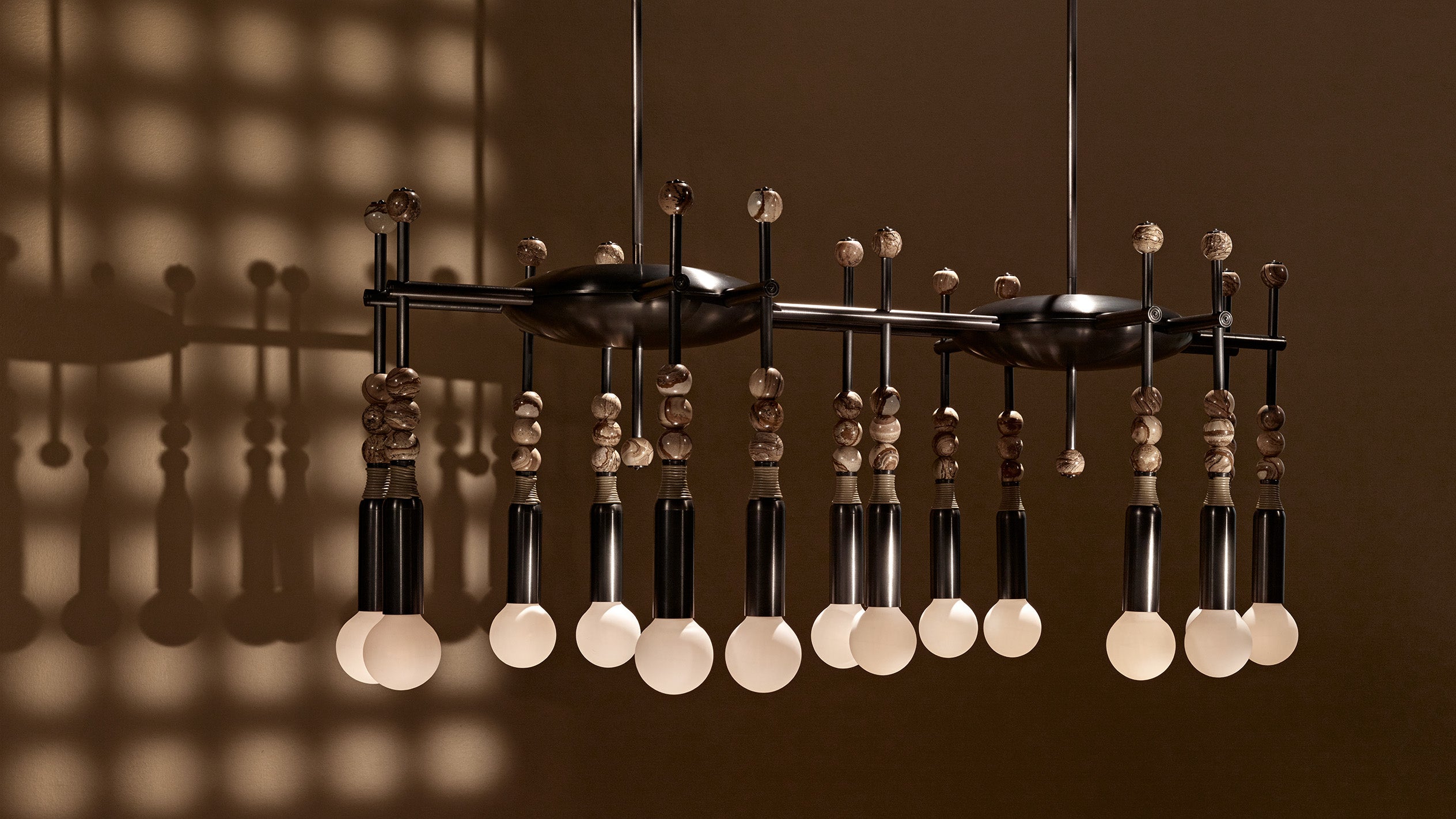 Modern black metal chandelier with wooden beads and round frosted bulbs casting grid shadows on brown wall