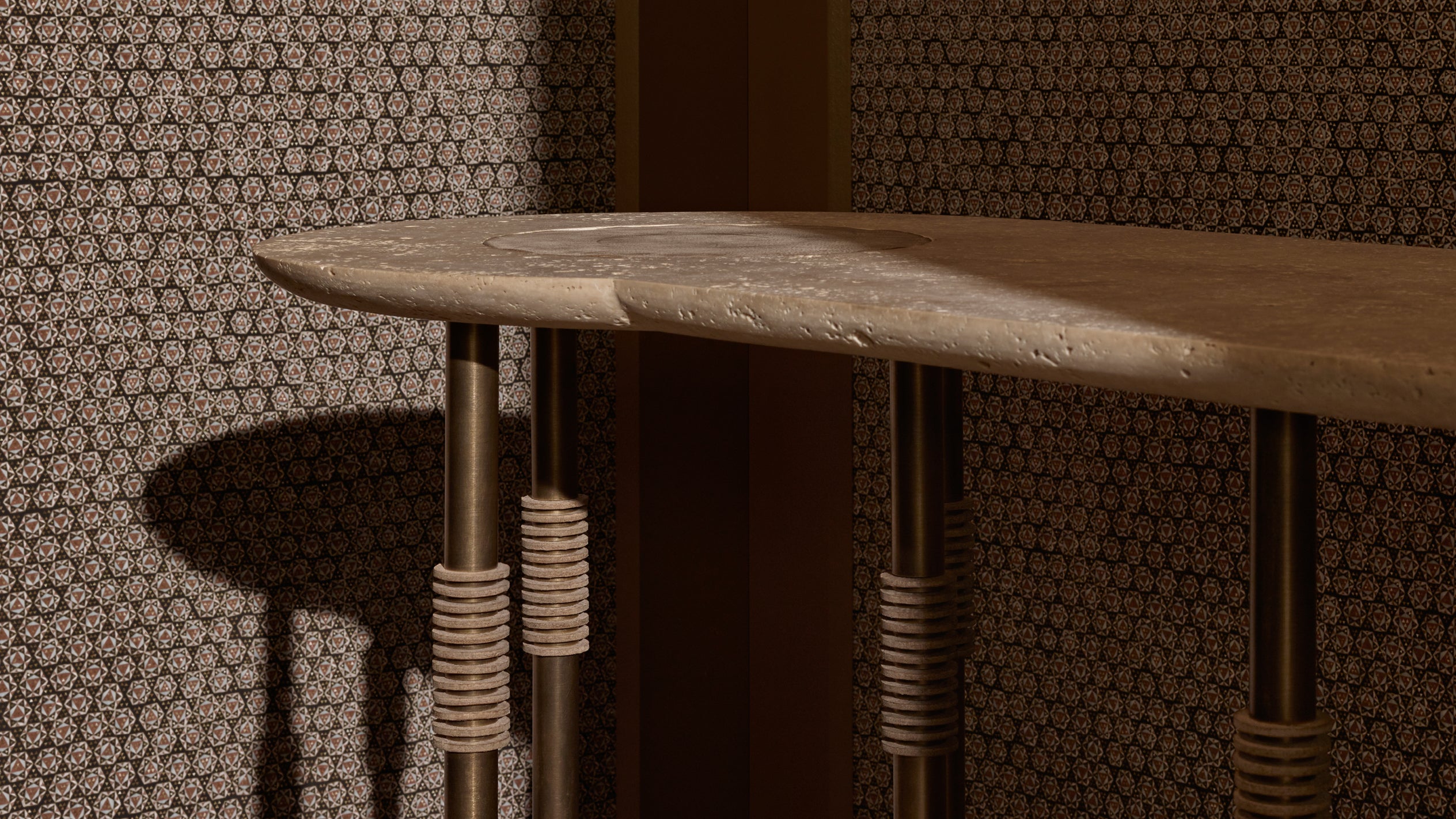 Close-up of a wooden table edge with cylindrical metal legs wrapped in textured rope against patterned wallpaper.