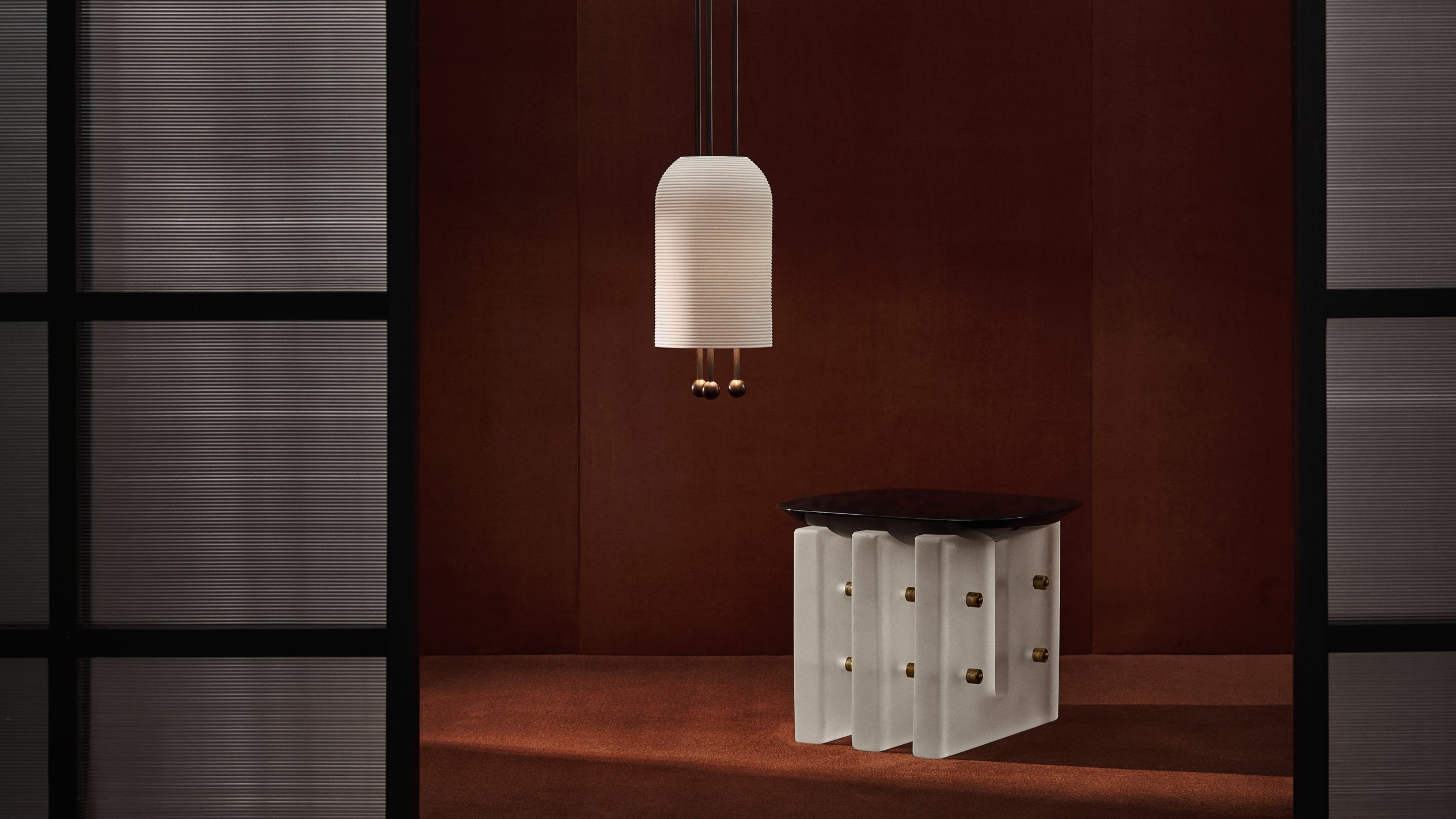 Modern white sculptural side table with gold accents beneath a pendant light against a rust-colored wall