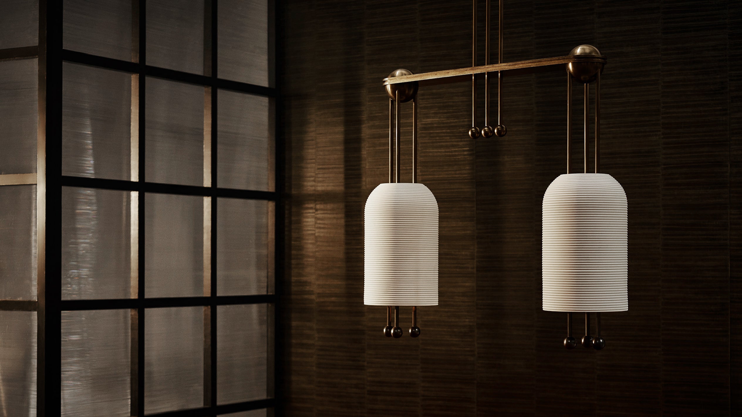 Pair of contemporary pendant lights with white ribbed shades hanging against a textured dark wall near a black-framed windowpane