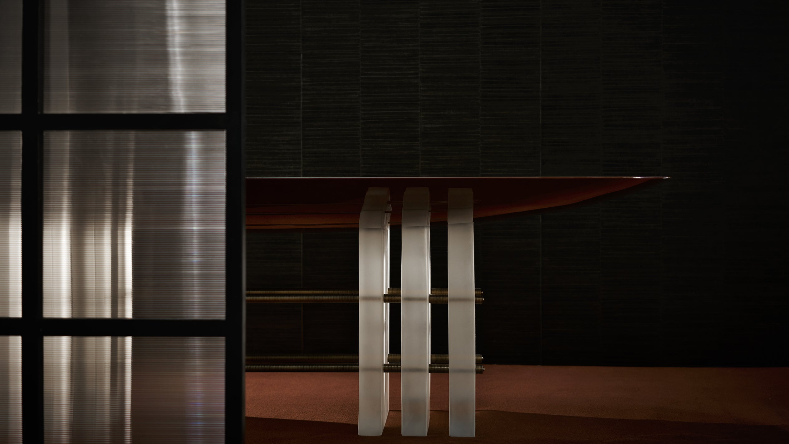 Side view of a modern table with a dark wood top and three translucent vertical supports against a dark textured wall