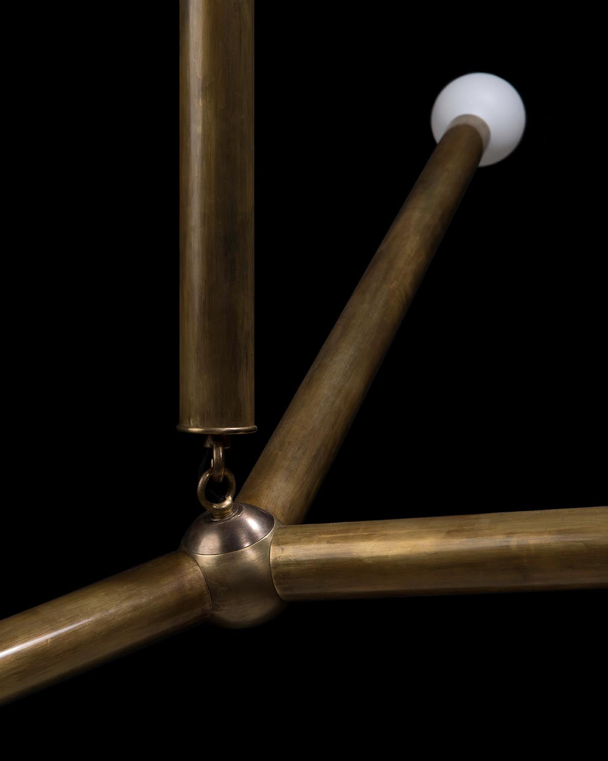 Close-up of brass rods joined at a central metal hub with a white spherical light at the end, against a black background