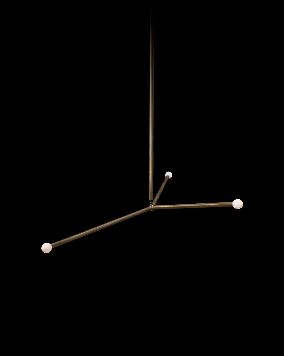 Minimalist modern chandelier with three brass arms and white spherical light bulbs against a black background