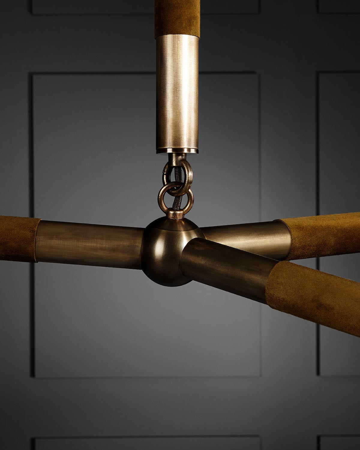 Close-up of a bronze and suede three-arm light fixture joint against a dark paneled wall background