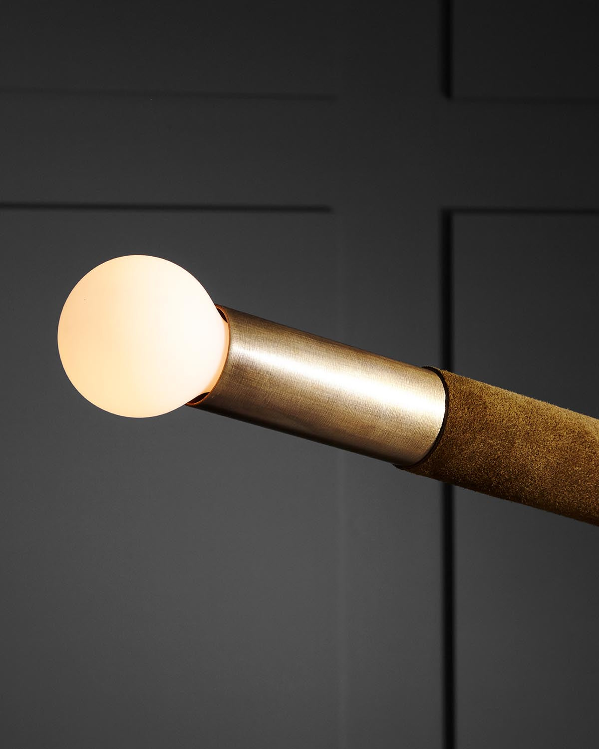 Close-up of a round frosted glass bulb on a brushed metal and textured brown cylindrical lamp arm against a dark background