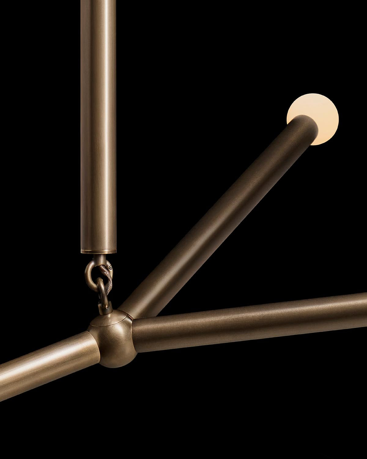 Close-up of bronze tubular metal rods connected by a central joint with one rod ending in a small round light against black background