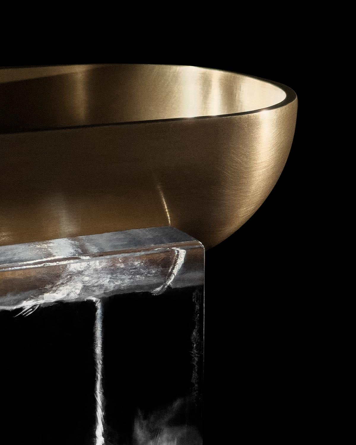 Close-up of a smooth metallic vessel with a brushed finish resting on a clear block against a black background