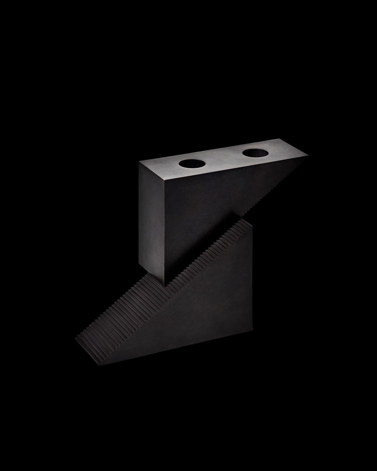 Minimalist black candle block with two circular holders and a textured slanted base on a black background