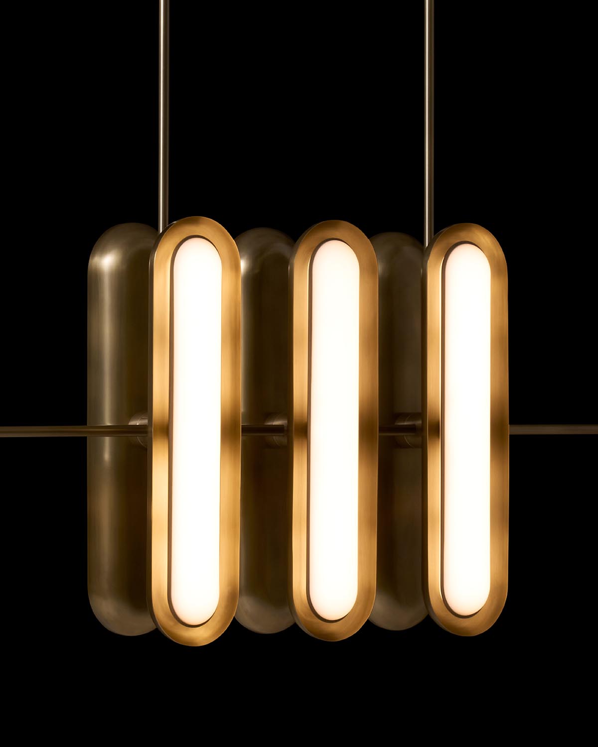 Close-up of three elongated oval brass pendant lights with soft glowing interiors against a black background