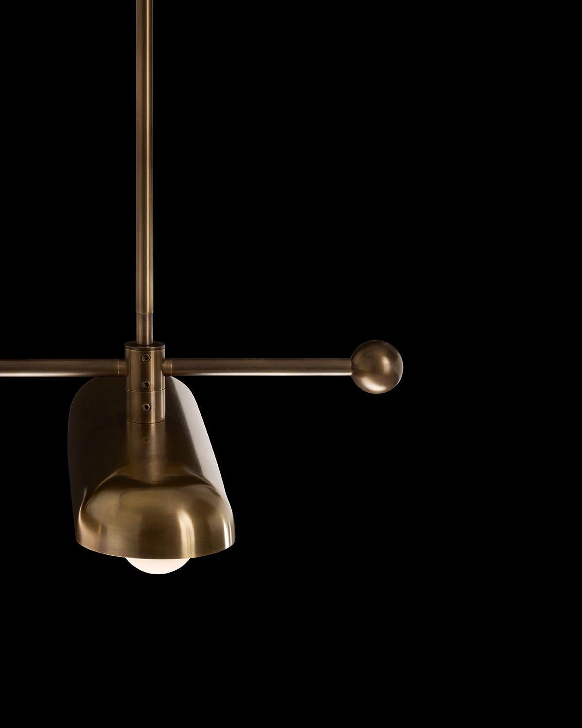 Close-up of a bronze cylindrical pendant light with spherical end details against a black background