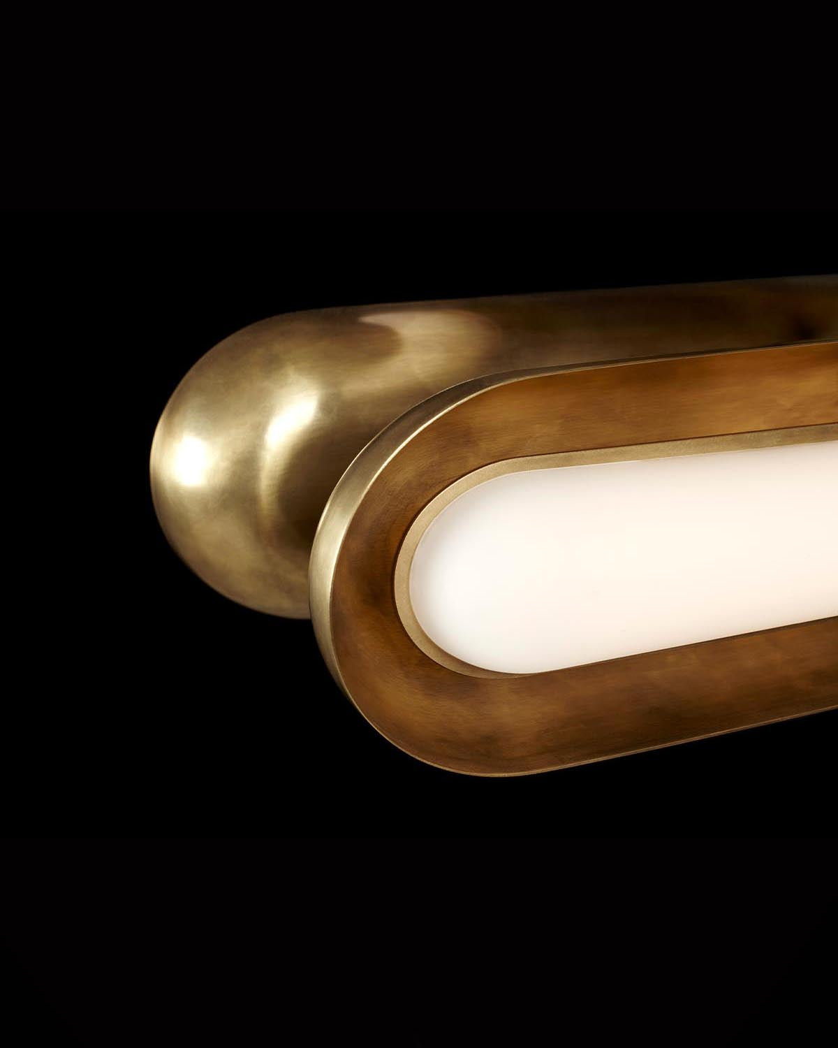 Close-up of an elongated oval brass light fixture with a smooth white diffuser against a black background