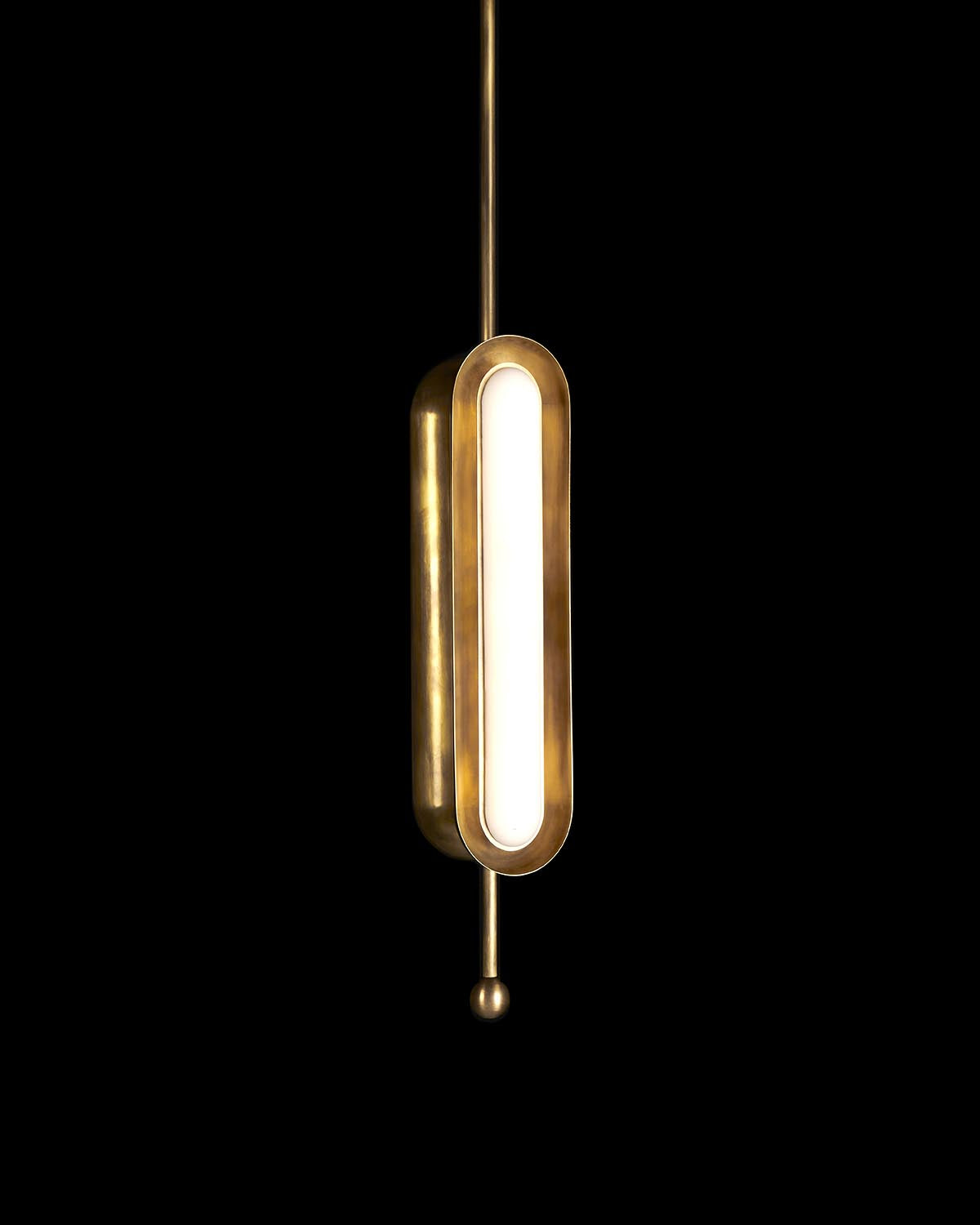 Vertical brass pendant light with elongated oval frosted glass diffuser against a black background