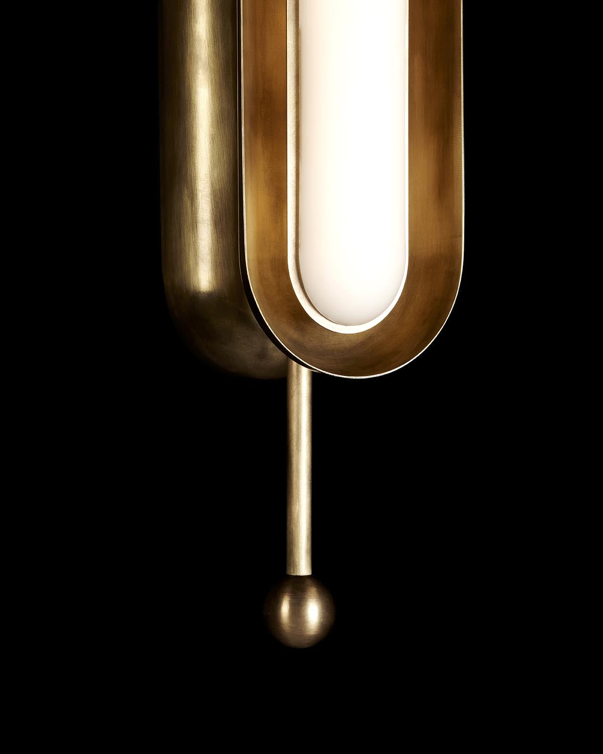 Close-up of vertical pendant light with brass frame and frosted glass diffuser against a black background