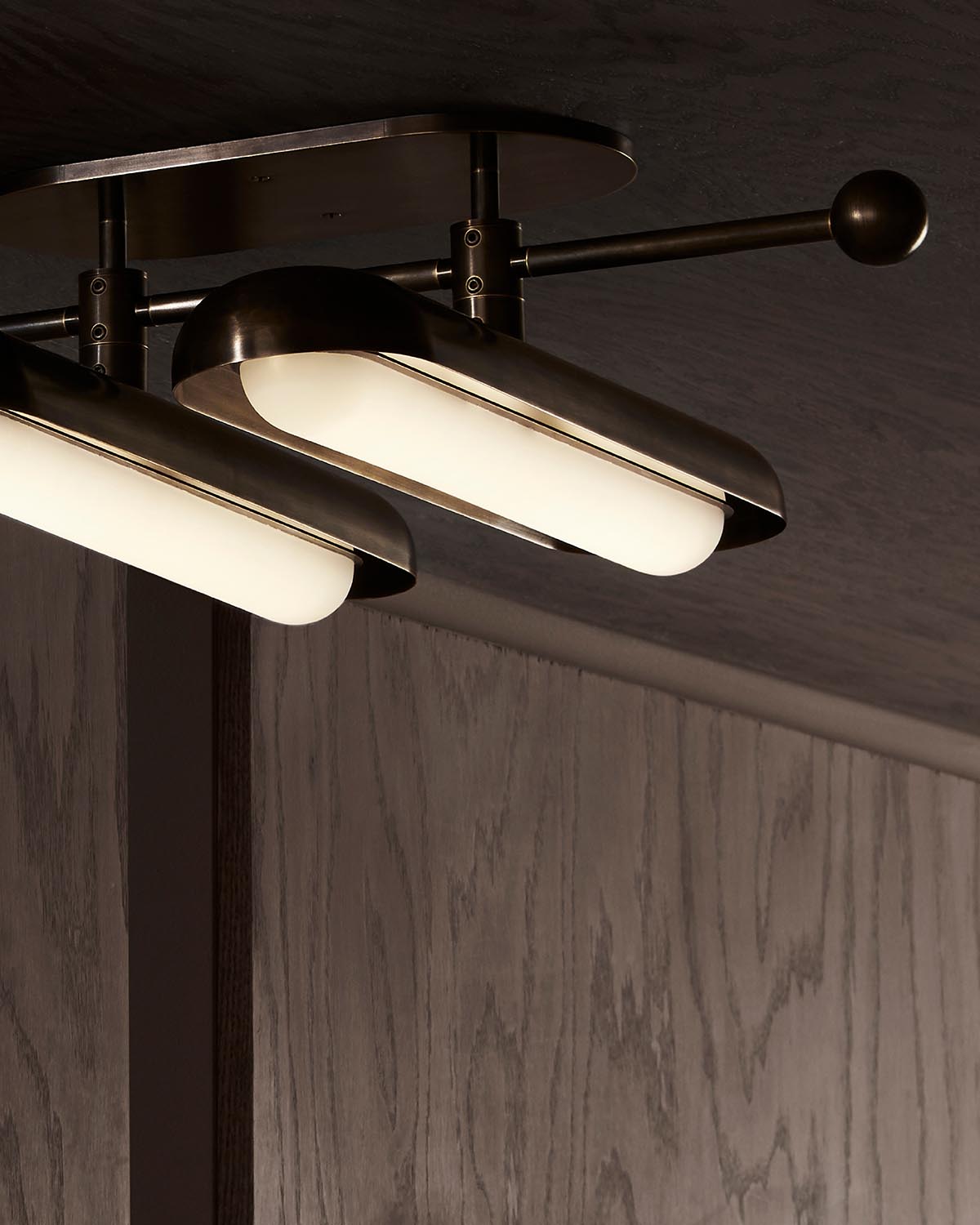 Close-up of modern ceiling light fixture with two elongated frosted glass shades and dark bronze metal frame