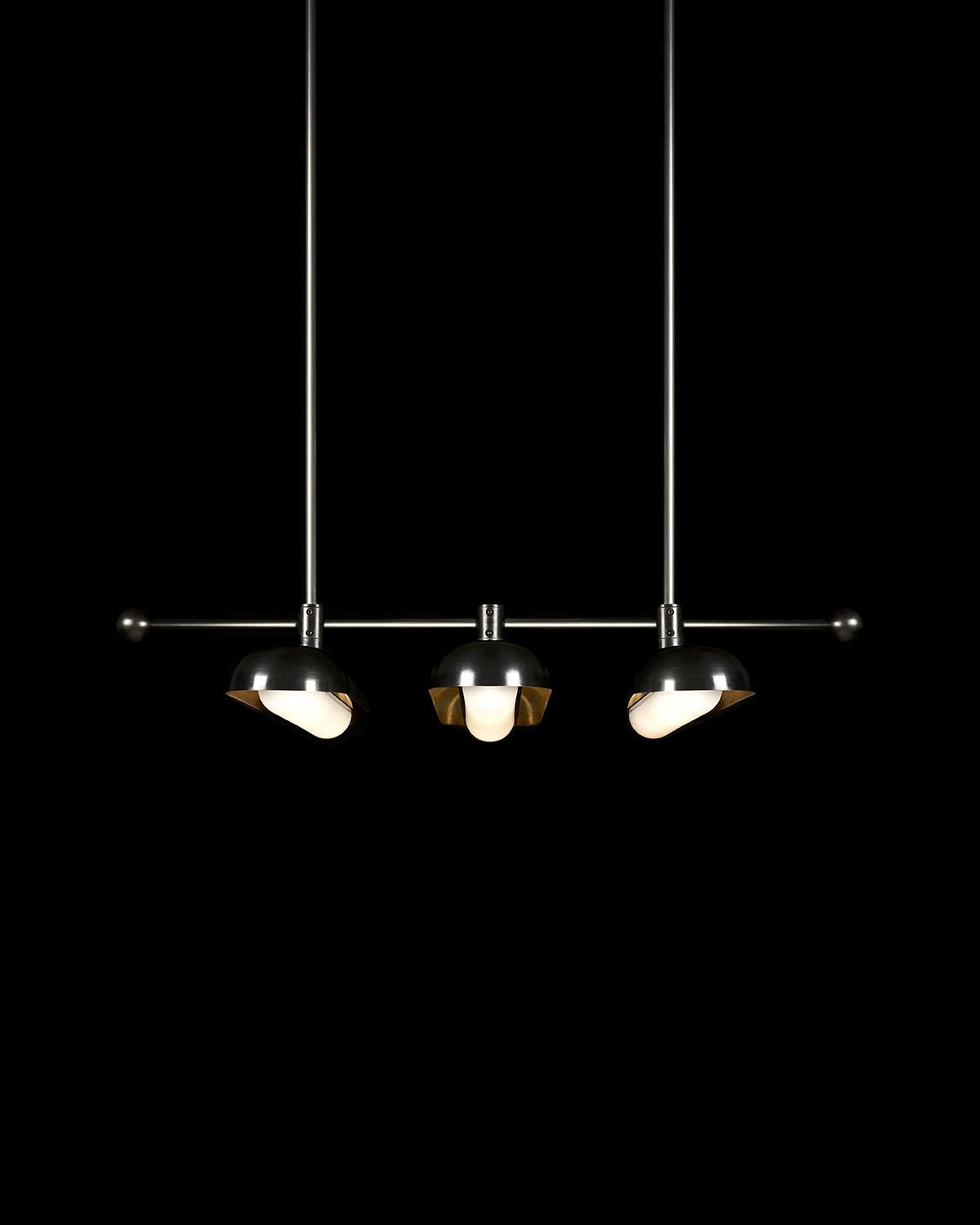 Minimalist three-pendant black metal light fixture with angled shades suspended on thin rods against a black background
