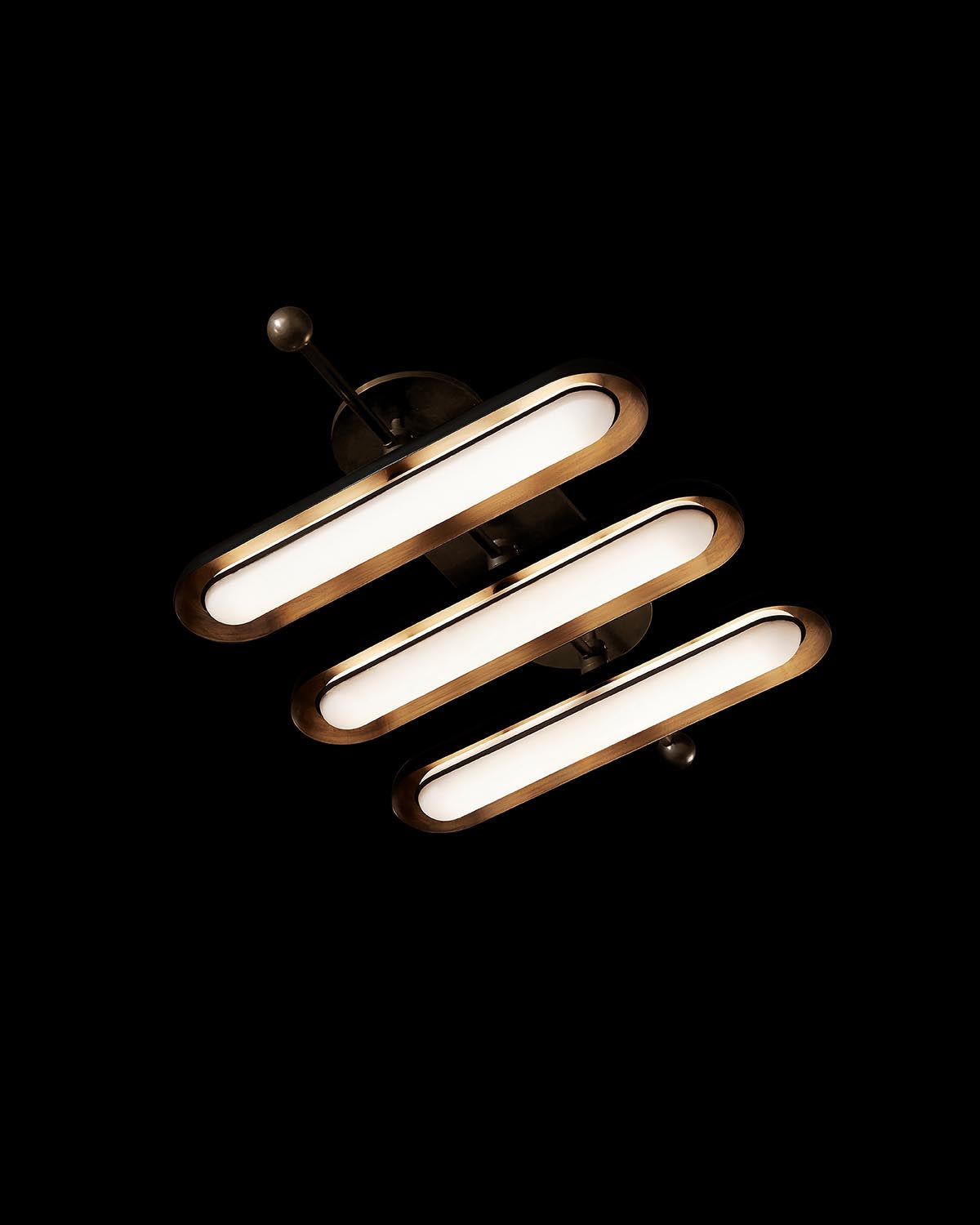 Modern ceiling light fixture with three elongated oval diffusers and bronze-toned metal accents on black background