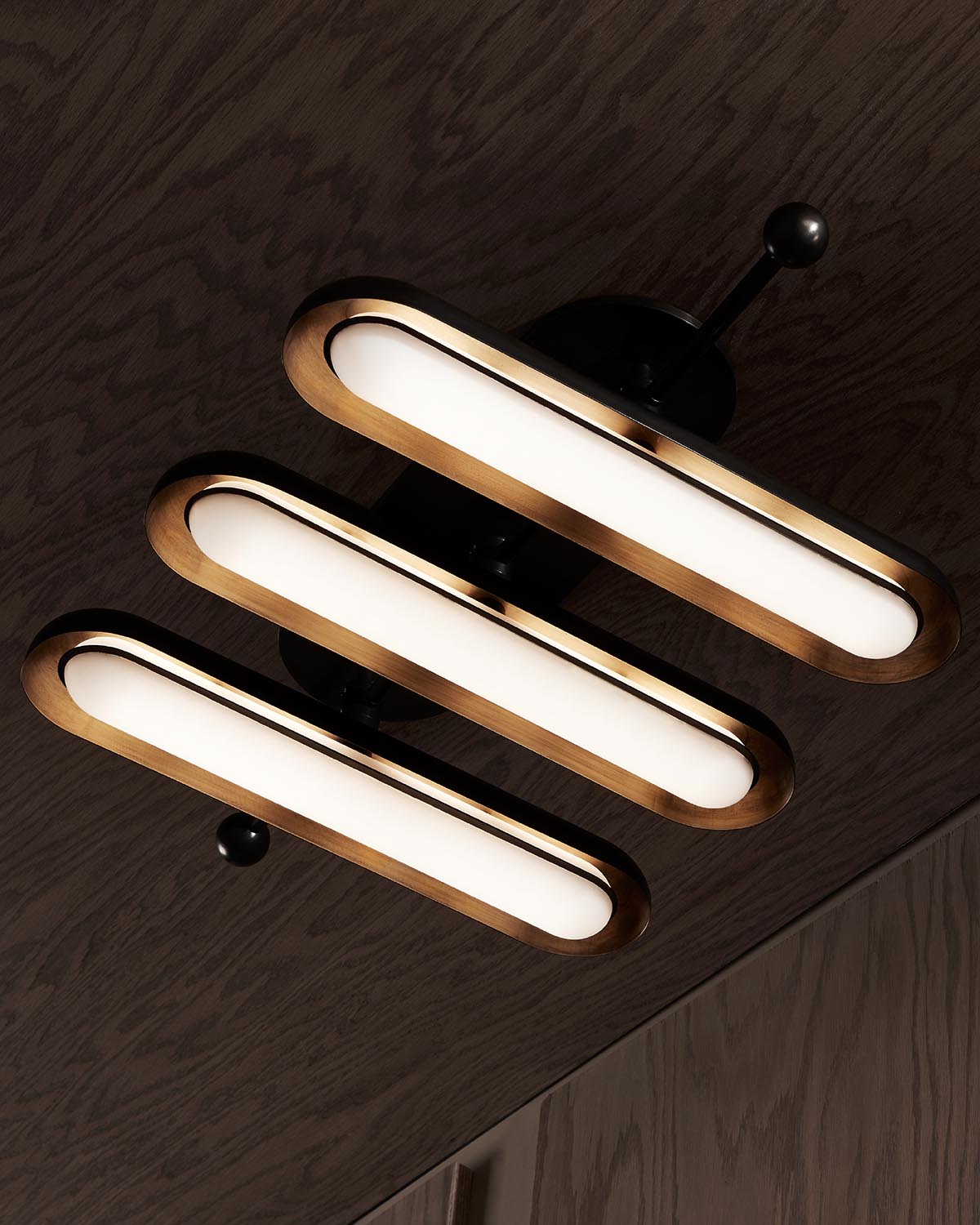 Three elongated oval light fixtures with warm brass edges mounted on a dark ceiling surface