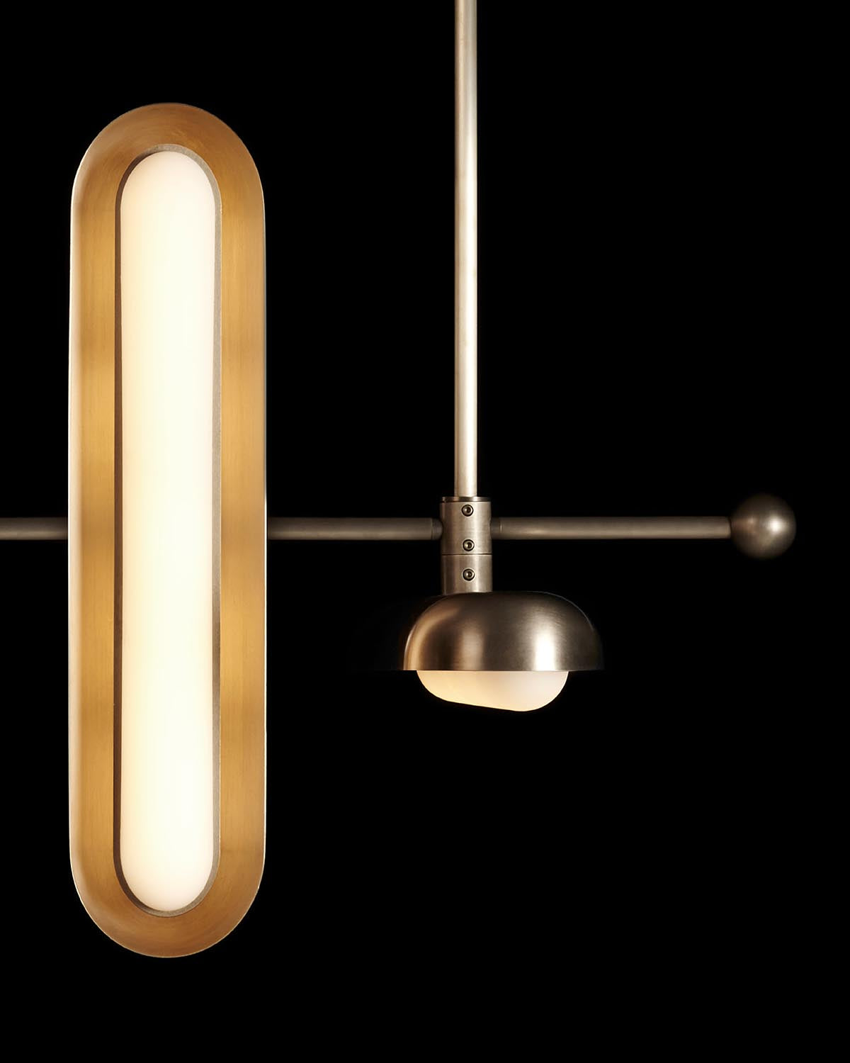Close-up of modern pendant light fixture with elongated brass oval and spherical dark metal shade on black background
