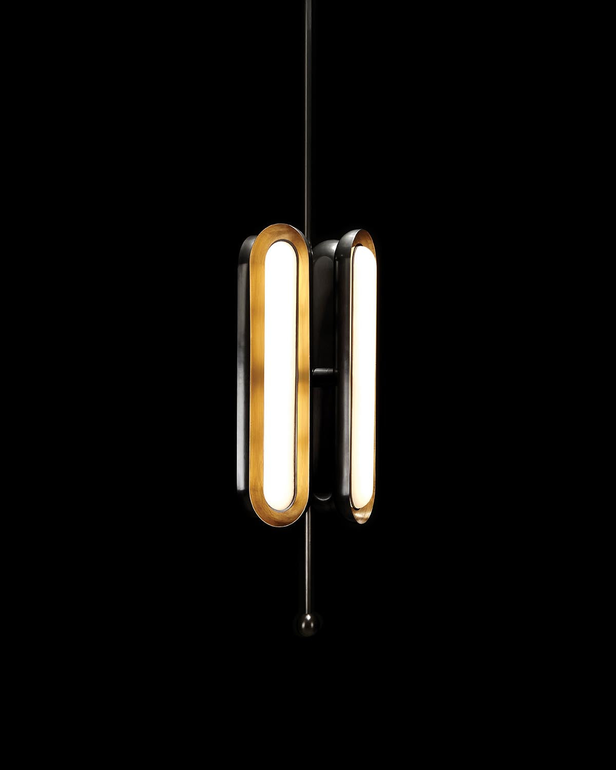 Vertical pendant light fixture with four elongated oval bulbs in gold and black finish against black background