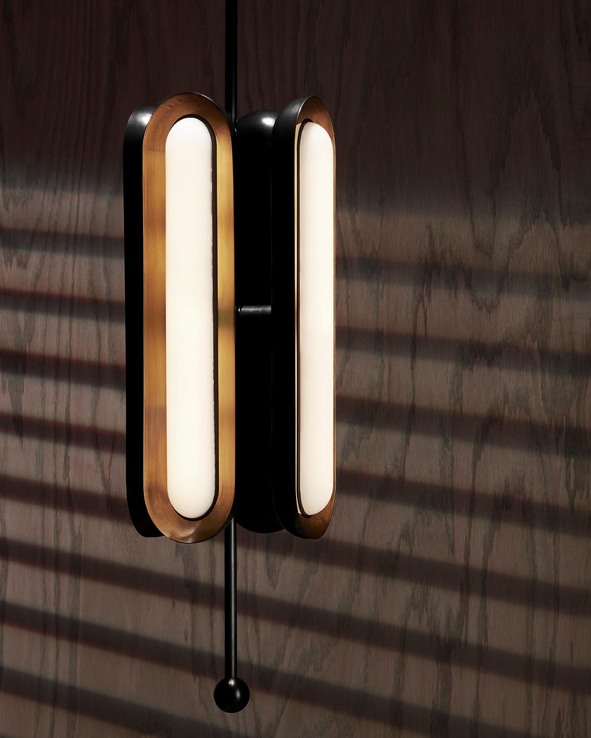 Close-up of CIRCUIT 4 Vertical pendant light with black and brass finishes against a dark wood background with shadows