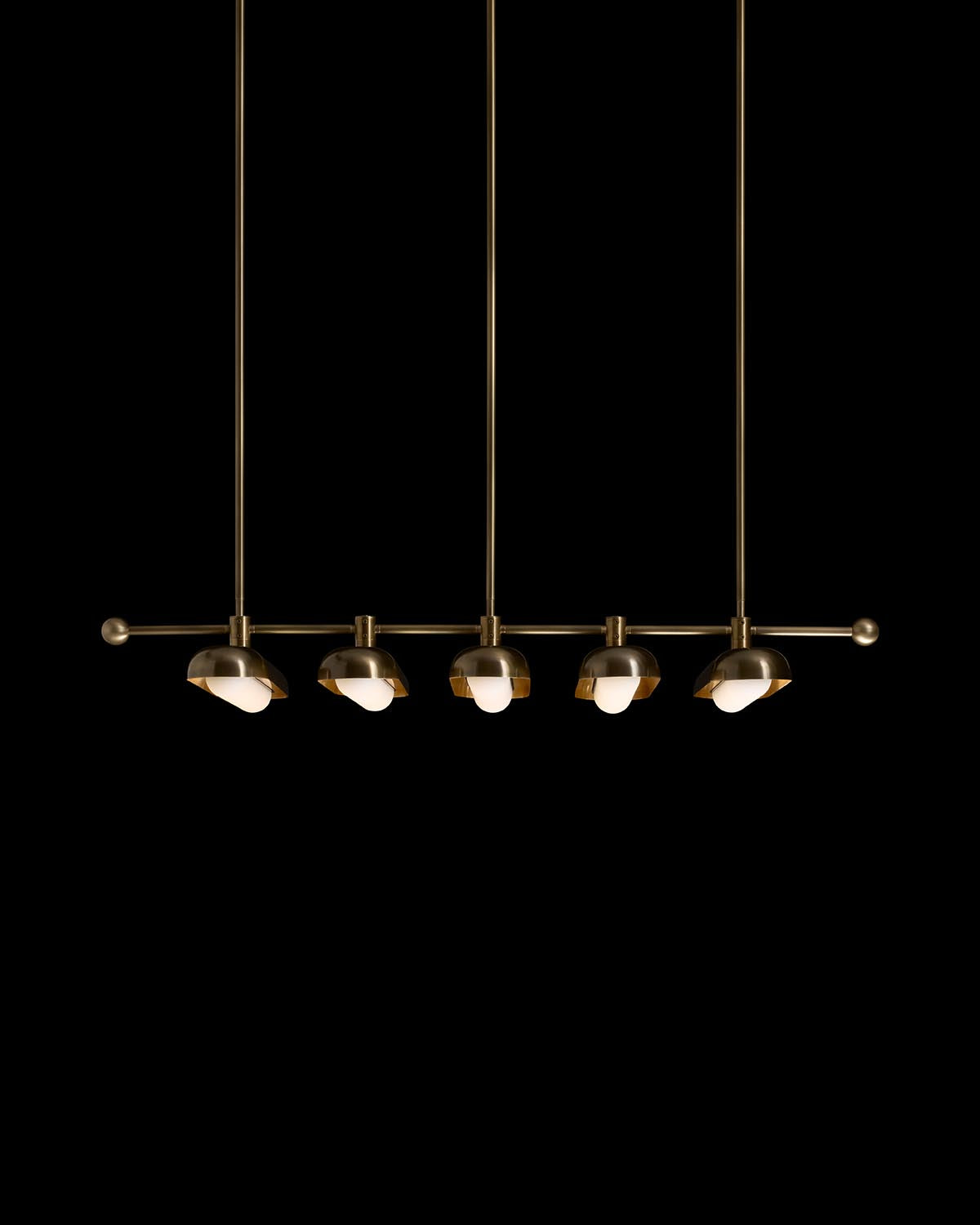 Linear pendant light with five spherical brass fixtures on a horizontal rod suspended by slim rods against a black background