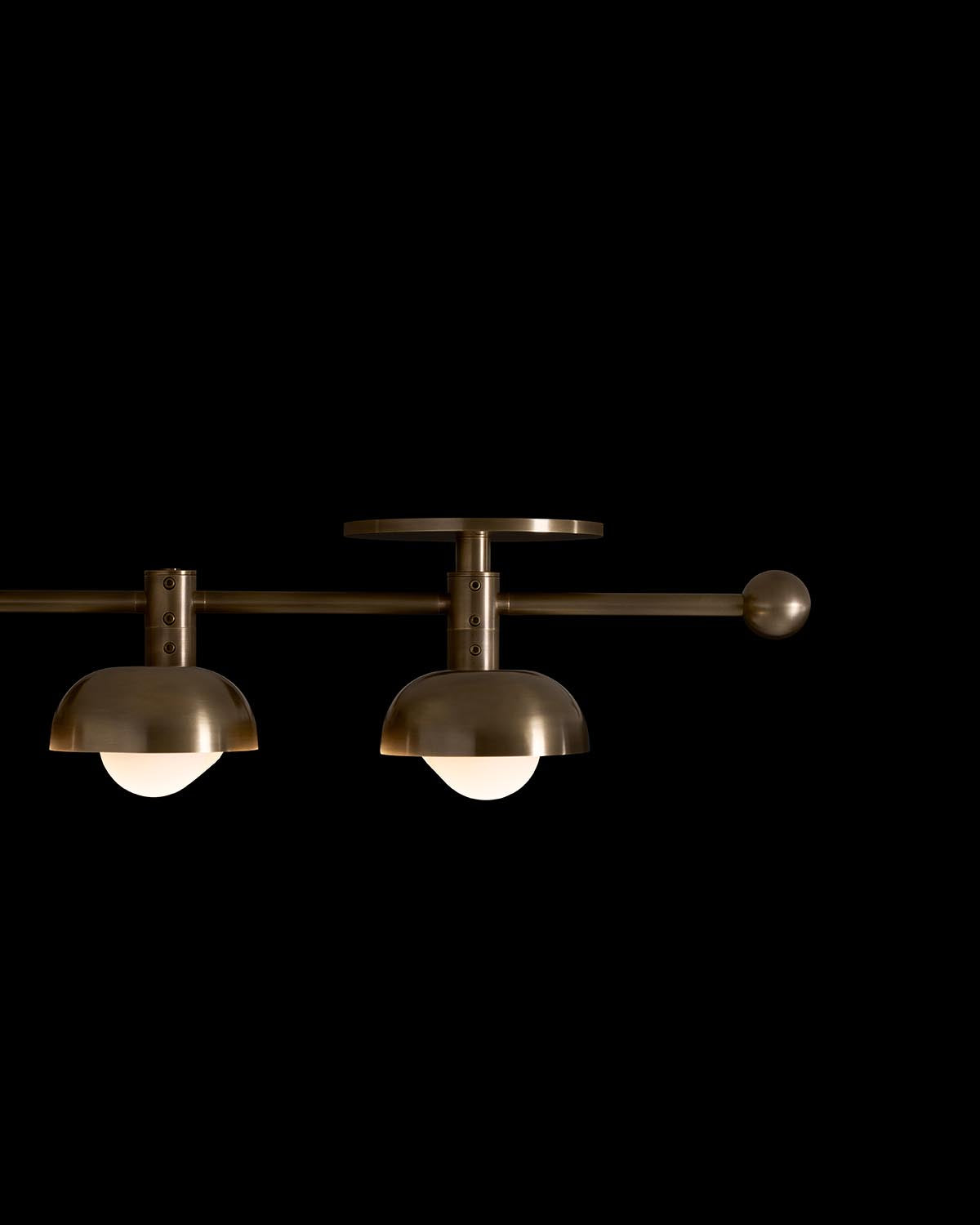 Close-up of a modern brass ceiling light fixture with two dome-shaped shades and frosted glass bulbs on black background