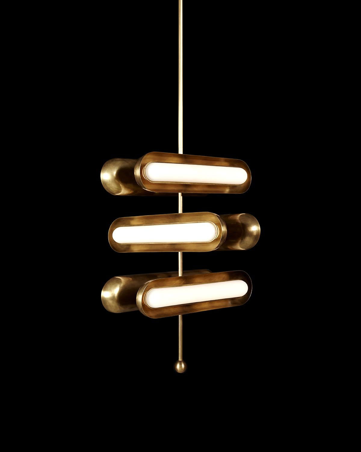 Modern pendant light fixture with three horizontal brass cylindrical lights on a central vertical rod against black background