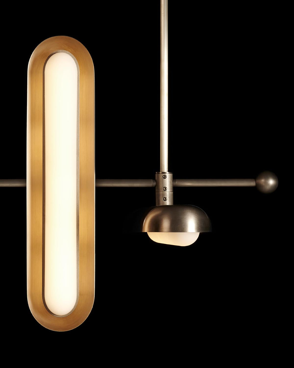 Close-up of modern pendant light fixture with elongated brass oval and matte metal dome against black background