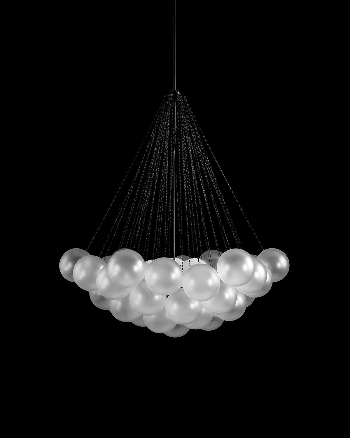 Modern chandelier with multiple frosted glass globes suspended by thin black cords against a black background
