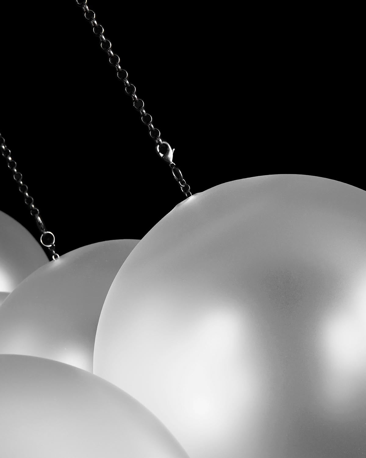 Close-up of frosted white spherical pendant lights suspended by black metal chains against a dark background
