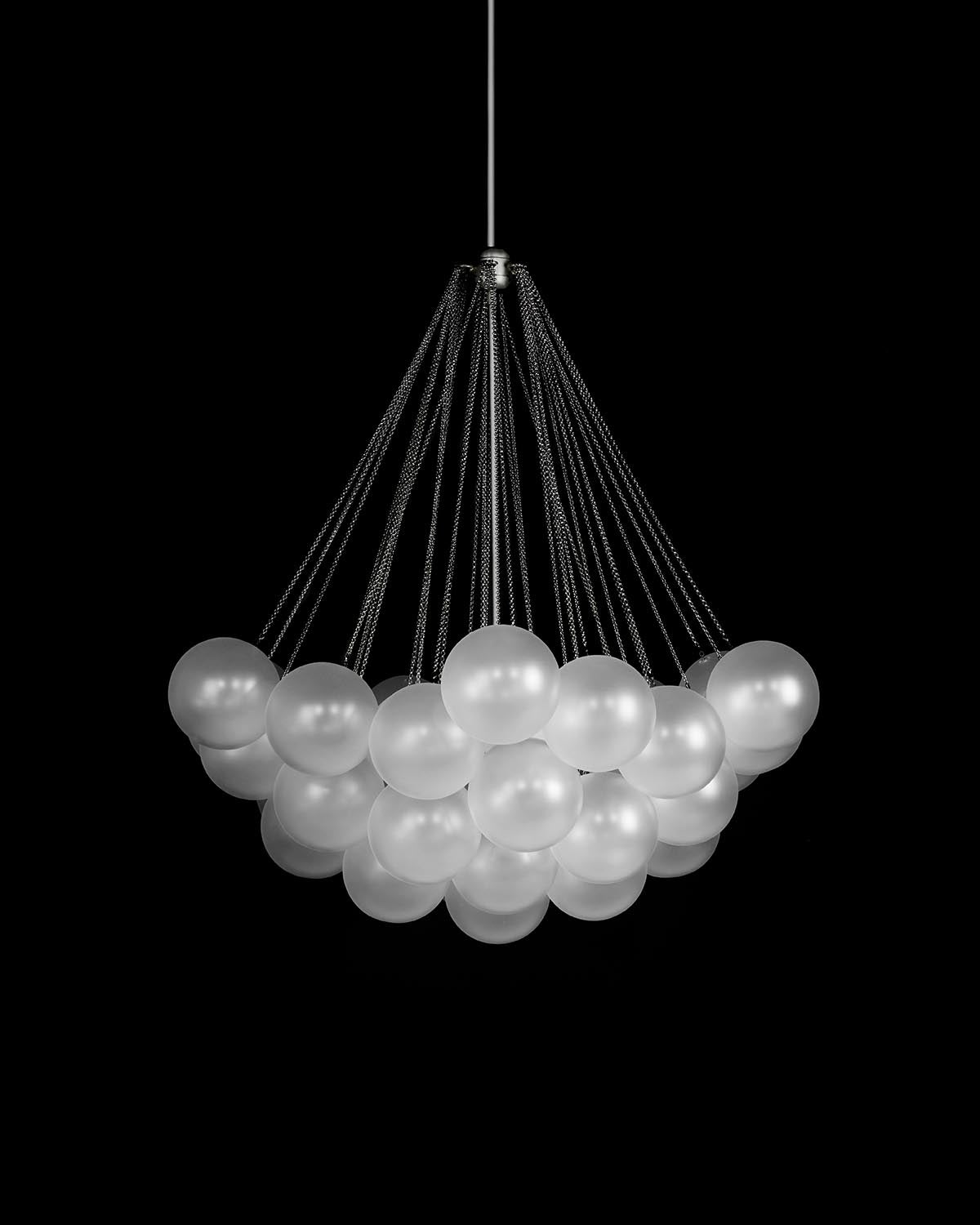 Suspended cluster chandelier with frosted glass spheres hanging from multiple black cords against a black background