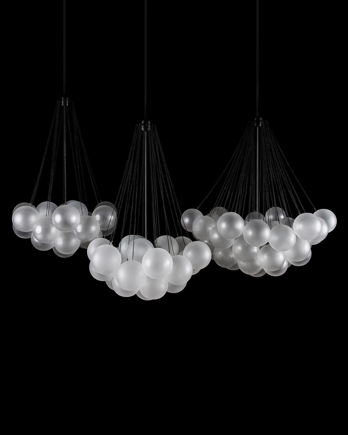 Three pendant light clusters of frosted glass spheres suspended by black cords against a dark background