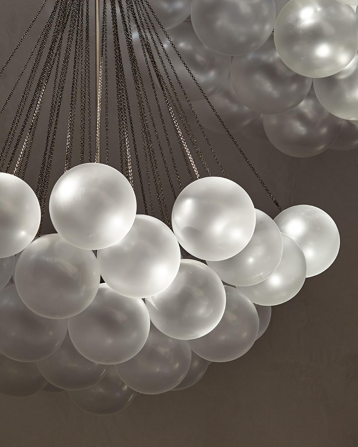 Cluster of frosted glass globe lights suspended by thin metal chains against a neutral background