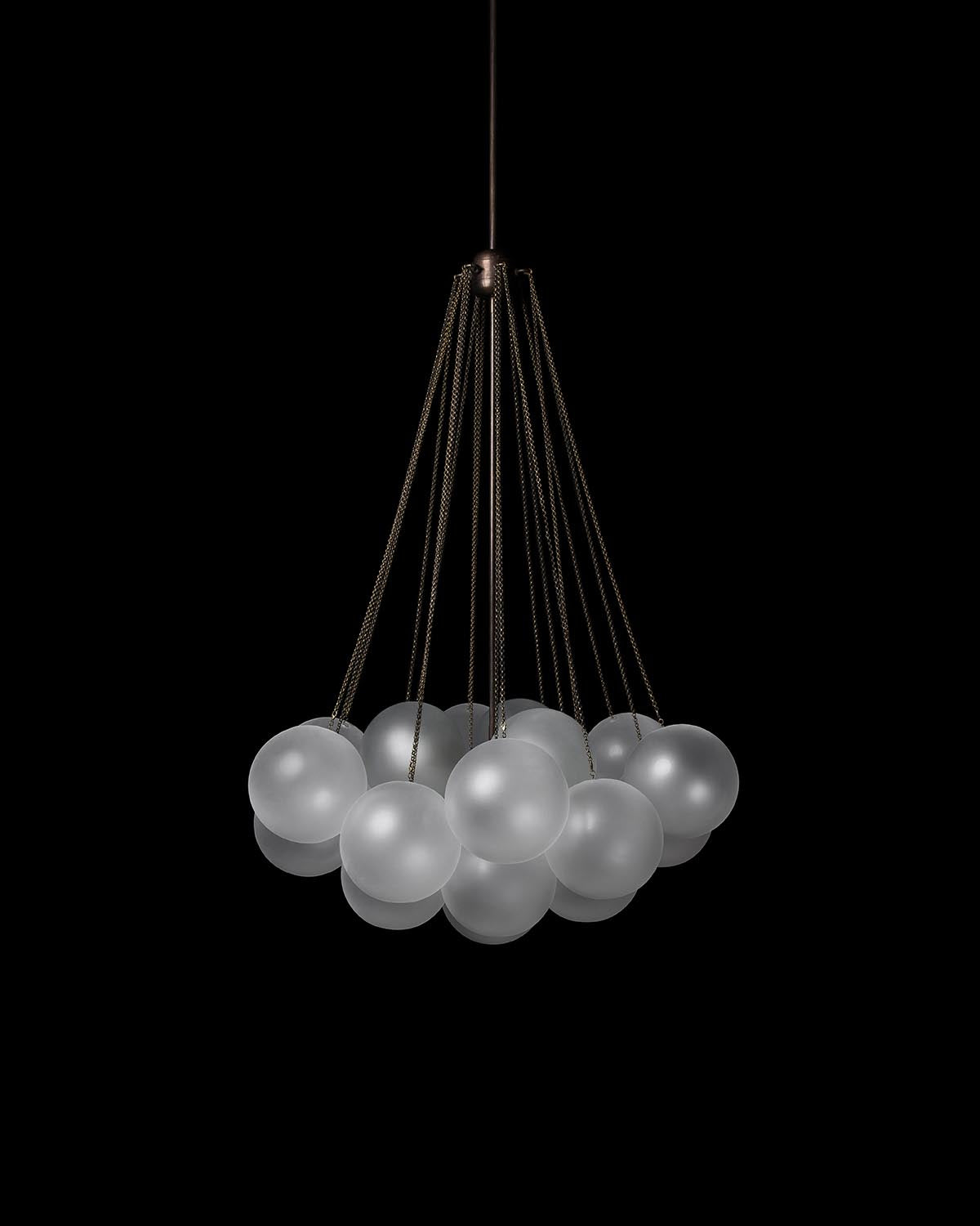 Cluster of frosted glass spherical pendants suspended by thin dark cords against black background
