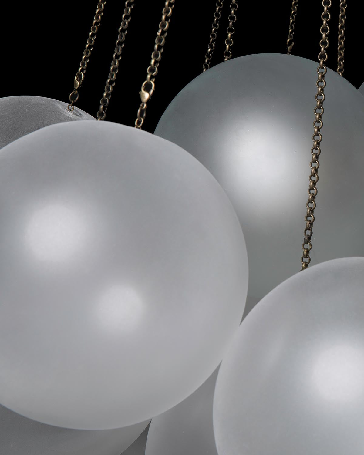 Cluster of large frosted glass globes suspended by thin antique brass chains against dark background