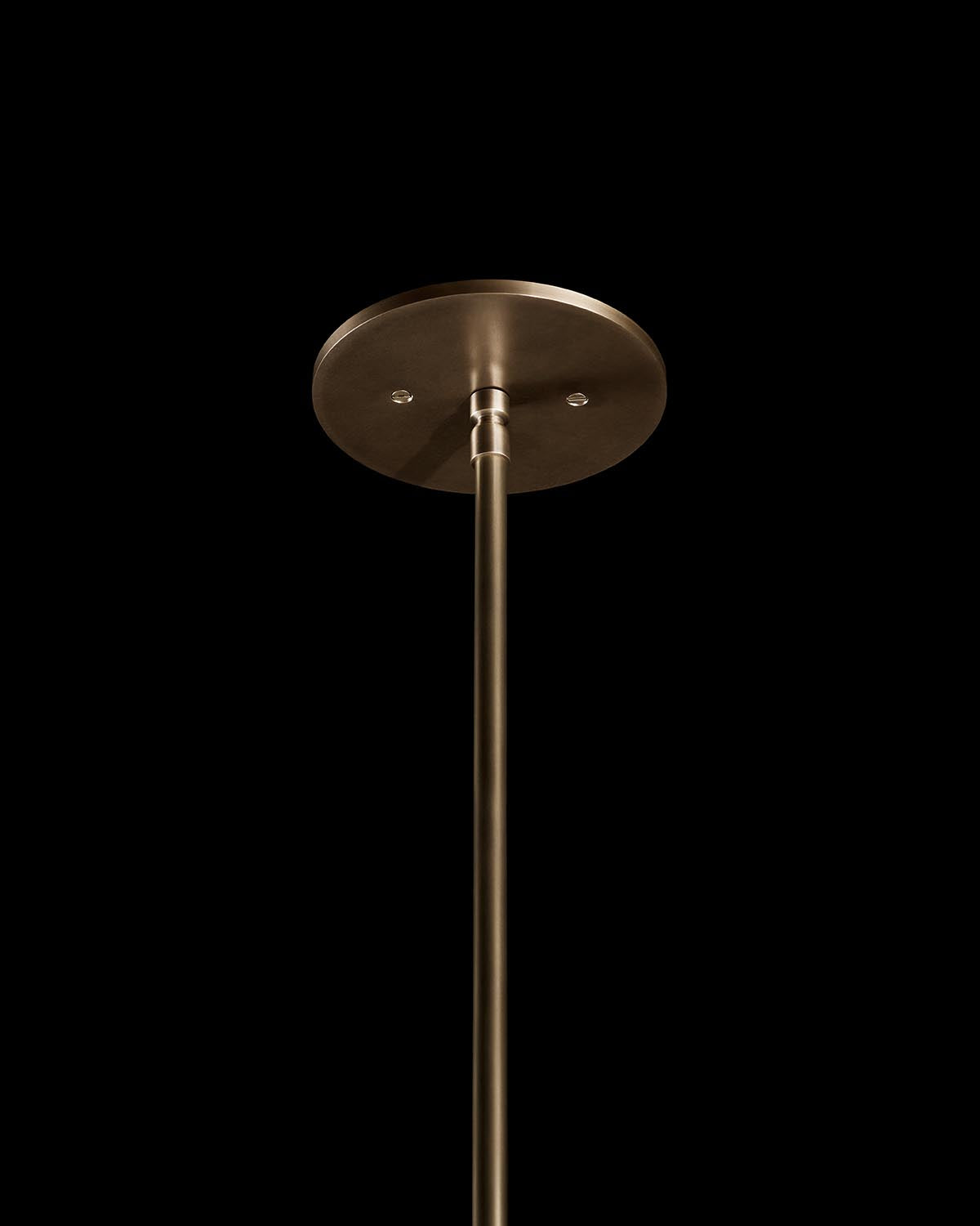 Ceiling mount and slender metal rod in a brushed brass finish against black background